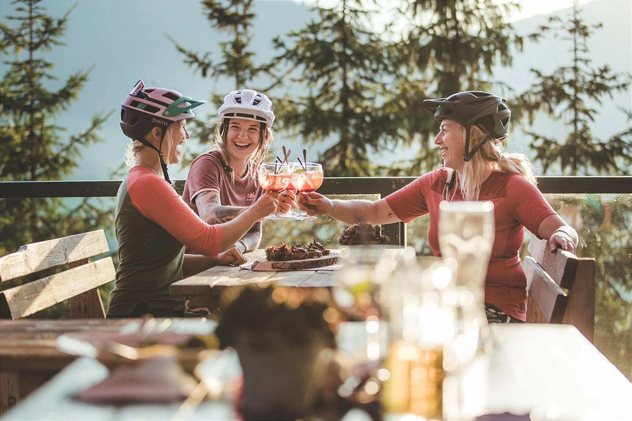 Bike Hotels © Hotel Sonnblick GmbH Drei Radfahrerinnen stoßen mit Getränken an auf einer Terrasse im Wald
