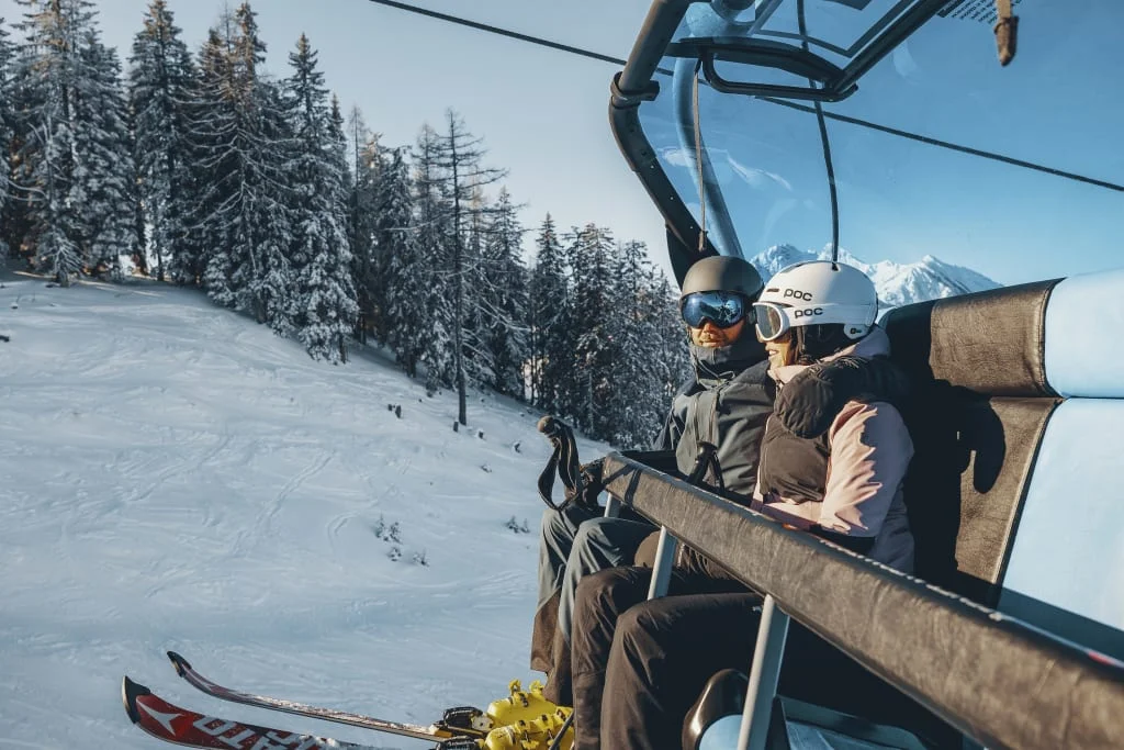 Zwei Skifahrer auf dem Sessellift mit verschneiten Bäumen im Hintergrund