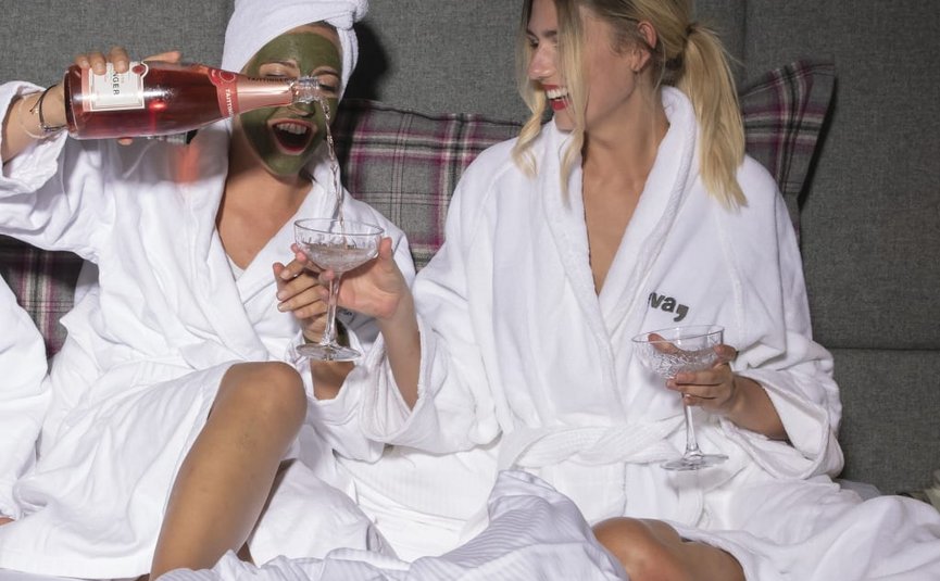 GIRLS SKI DREAM Zwei Frauen im Bademantel genießen einen Spa-Abend mit Gesichtsmaske und Getränken