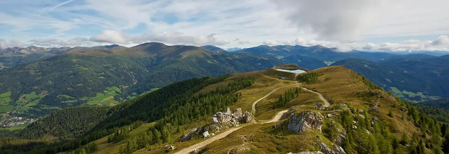 Mountain path with green forest and mountains under cloudy sky