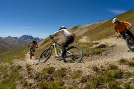 Drei Mountainbiker fahren einen kurvigen Bergpfad bei klarem Himmel hinunter