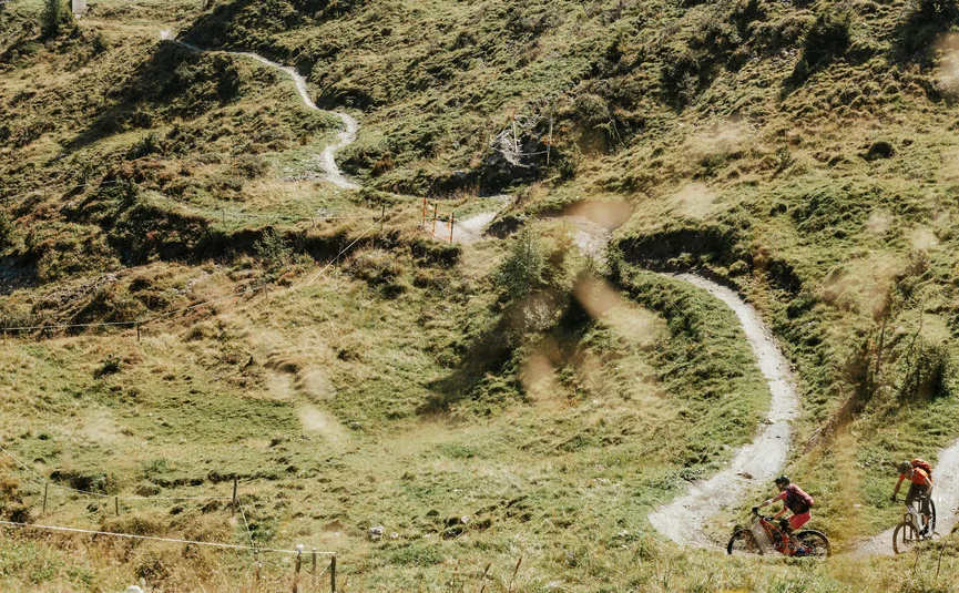 Zwei Mountainbiker auf einem kurvigen Pfad in hügeliger Landschaft