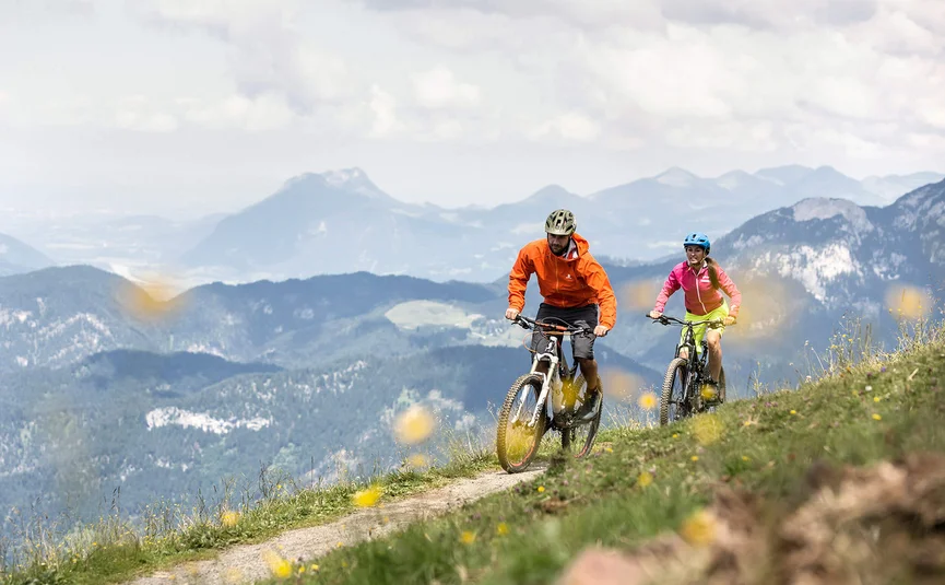 Two mountain bikers cycling on a mountain trail with mountains in the background
