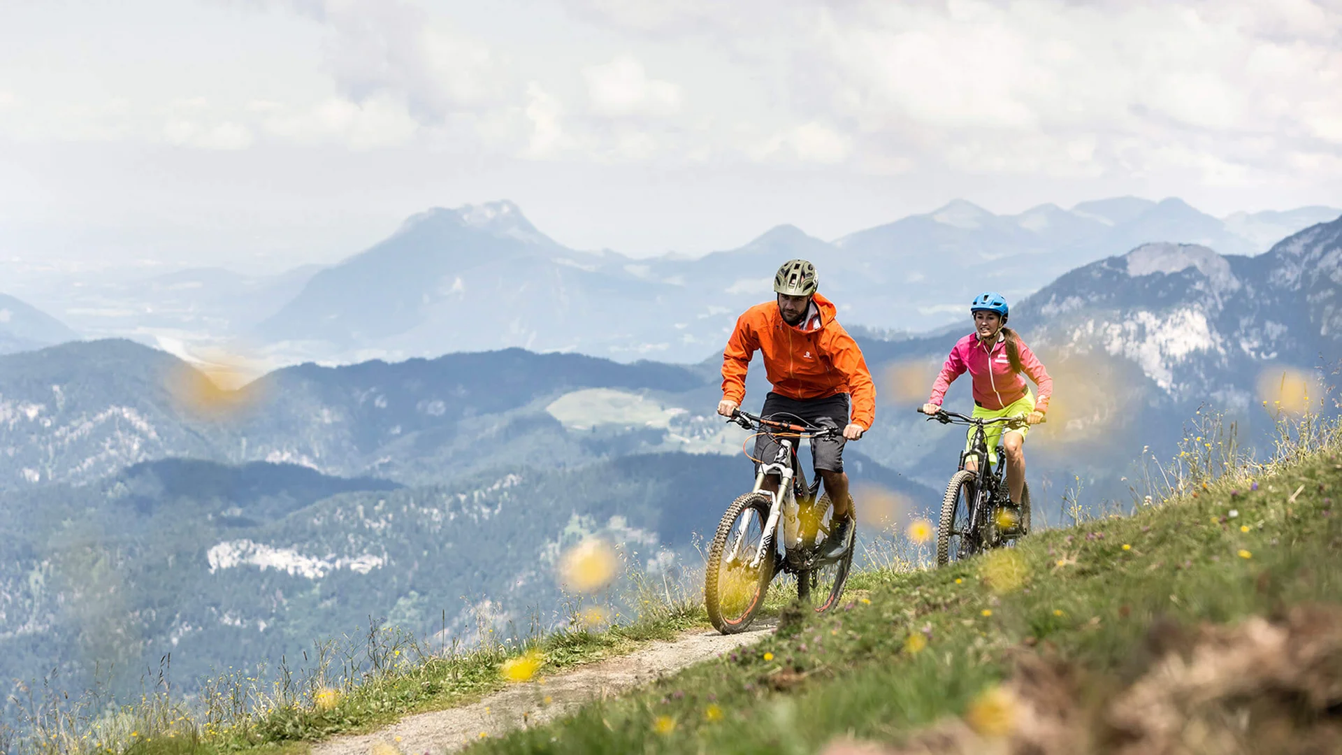 Zwei Mountainbiker fahren auf einem Bergweg mit Bergen im Hintergrund