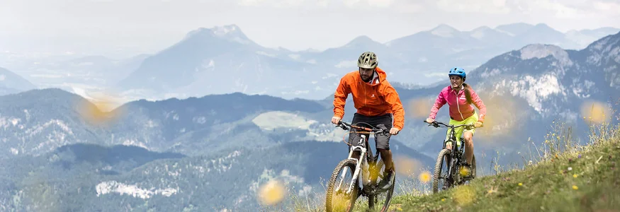 Two mountain bikers cycling on a mountain trail with mountains in the background