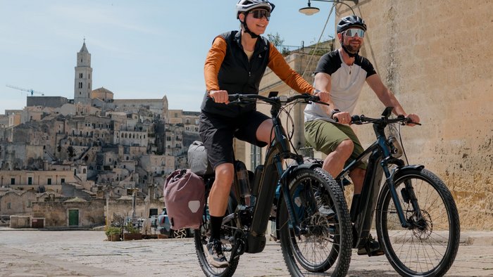 Zwei Radfahrer mit Helmen fahren auf Kopfsteinpflaster in einer alten Stadt