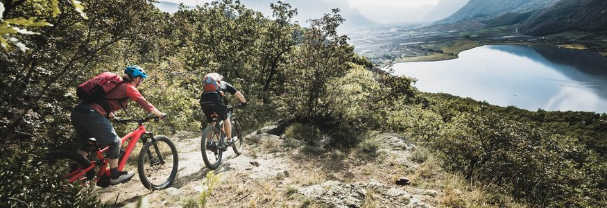 Traminerhof | good life. cool ride. © Mia Knoll Two mountain bikers riding on a forest trail with lake and mountains view