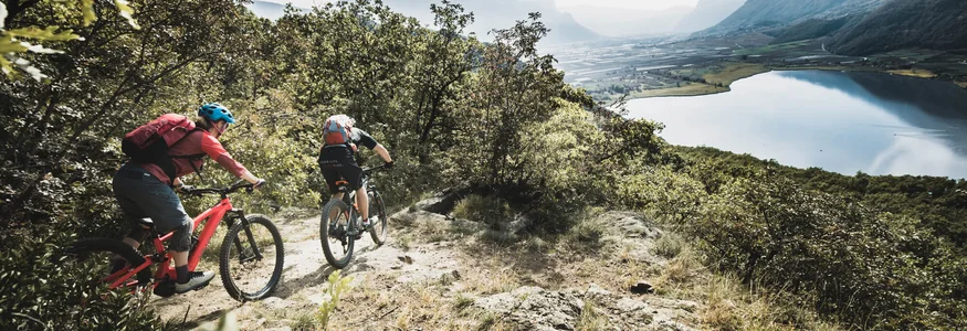 Two mountain bikers riding on a forest trail with lake and mountains view