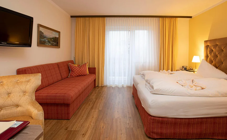 Gezellige hotelkamer met rode bank, tweepersoonsbed en tv aan de muur