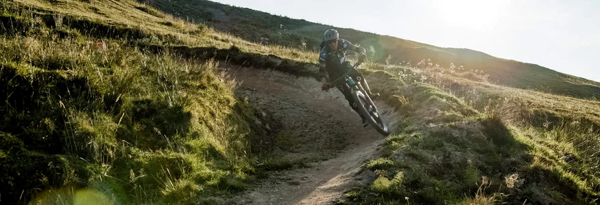 Mountainbiker in voller Ausrüstung auf kurvigem Trail bei Sonnenlicht