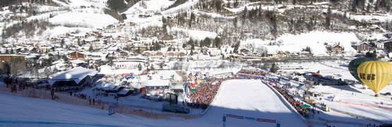 Relax und Aktiv Tage Besneeuwde skipiste met uitzicht op een stad in de bergen met toeschouwers en luchtballonnen