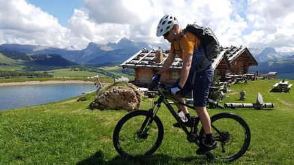 Fietser met helm bij berghuisjes en meer onder zonnige lucht