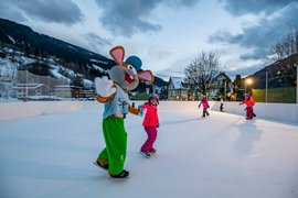 Kinderen schaatsen met een muismascotte op een buitenbaan in een besneeuwd bergdorp