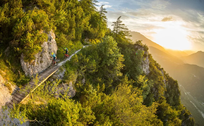 Two mountain bikers on narrow mountain trail at sunset