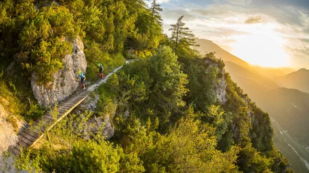 Zwei Mountainbiker auf schmalem Bergpfad bei Sonnenuntergang