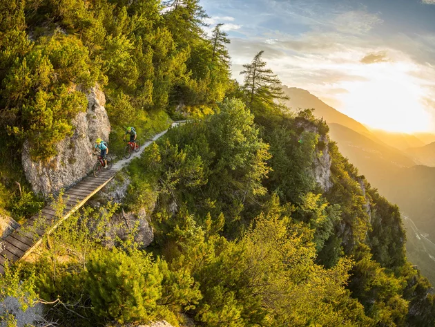 Zwei Mountainbiker auf schmalem Bergpfad bei Sonnenuntergang