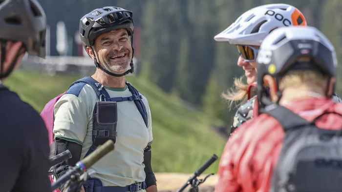 Gruppe fröhlicher Mountainbiker in Helm und Schutzkleidung im Grünen