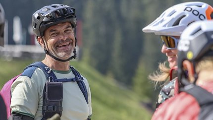 Gruppe fröhlicher Mountainbiker in Helm und Schutzkleidung im Grünen