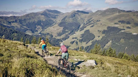 Zwei Mountainbiker fahren auf einem Pfad in den Bergen bei klarem Himmel