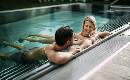 Couple swimming in a pool as the woman smiles at the pool edge