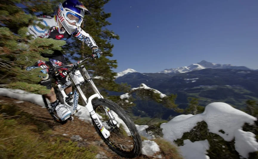 Mountain biker riding on a snowy mountain trail with mountains in the background