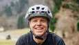 Lächelnder Radfahrer mit Schutzhelm auf Waldweg im Freien