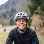 Lächelnder Radfahrer mit Schutzhelm auf Waldweg im Freien