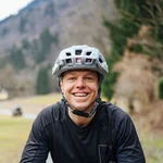 Lächelnder Radfahrer mit Schutzhelm auf Waldweg im Freien