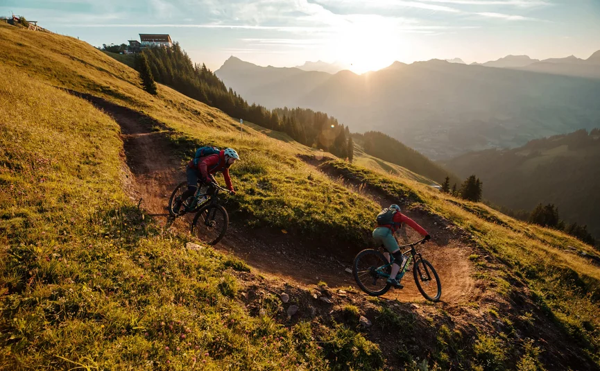 Hahnenkamm Trail © David Karg Zwei Mountainbiker fahren auf einem Bergpfad bei Sonnenuntergang