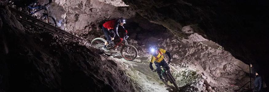 Mountain bikers riding through a lit tunnel inside a cave at night