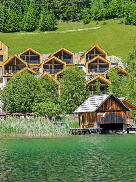 Holzferienhäuser am See mit grünen Bäumen und Hügeln im Hintergrund