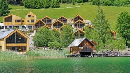 Holzferienhäuser am See mit grünen Bäumen und Hügeln im Hintergrund
