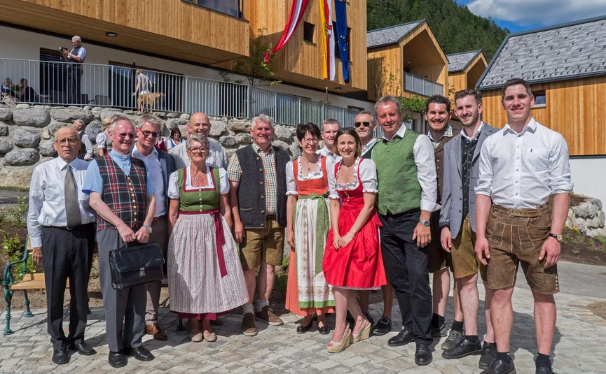 Gruppe von Menschen in traditioneller Tracht vor Holzgebäuden mit Fahnen