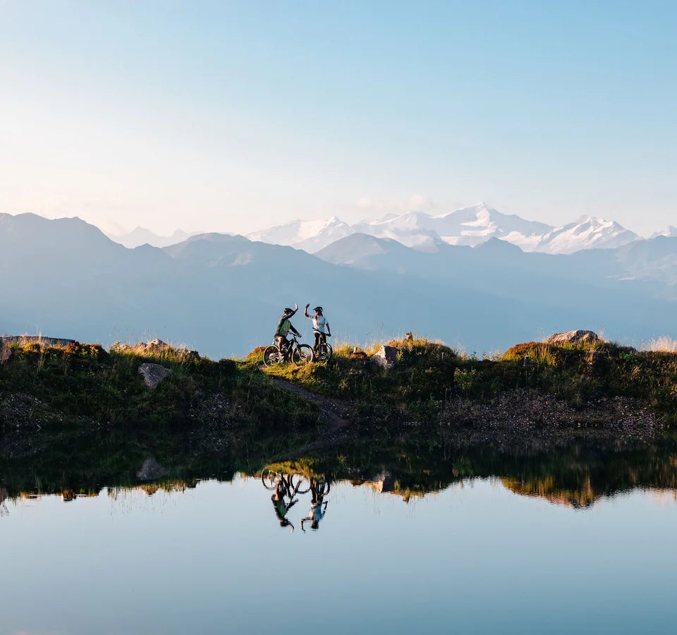Welcher Hohe Salve-MTB-Typ bist du? © Mathäus Gartner Zwei Mountainbiker feiern mit Bergblick am Seeufer