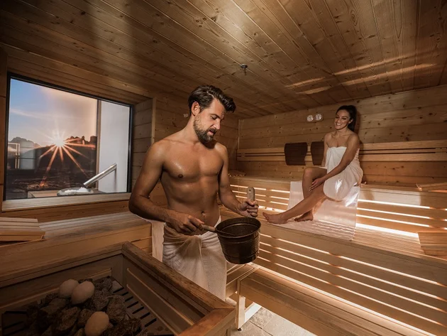 Man and woman relaxing in wooden sauna at sunset