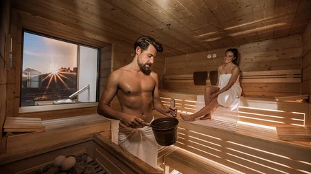 Man and woman relaxing in wooden sauna at sunset
