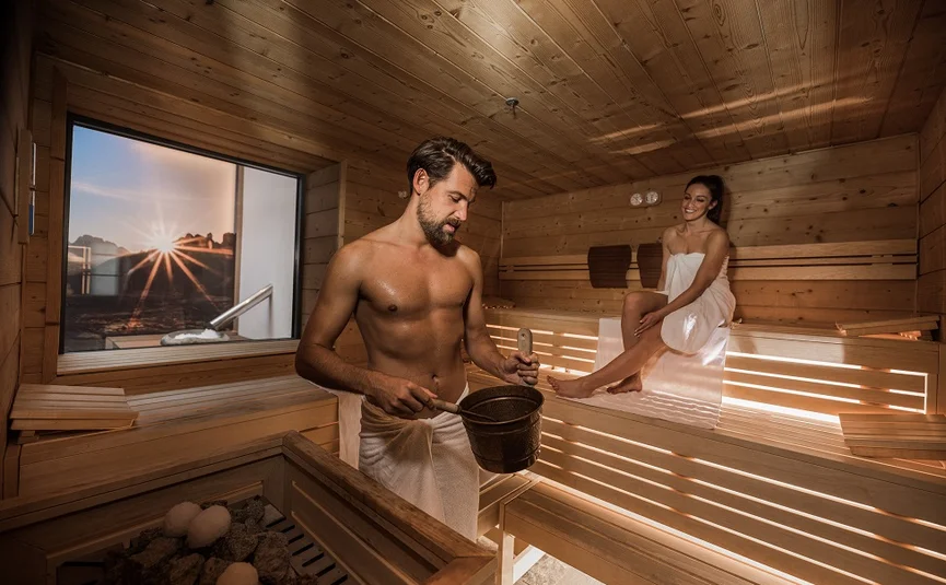 Man and woman relaxing in wooden sauna at sunset