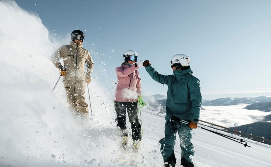 SUPER SKI Days Three skiers fist bump on snowy mountain slope