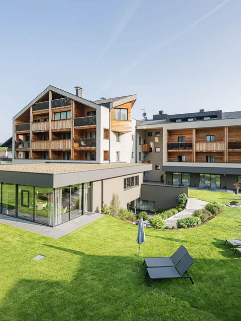 Modernes Hotel mit Liegestühlen im Garten und Bergen im Hintergrund