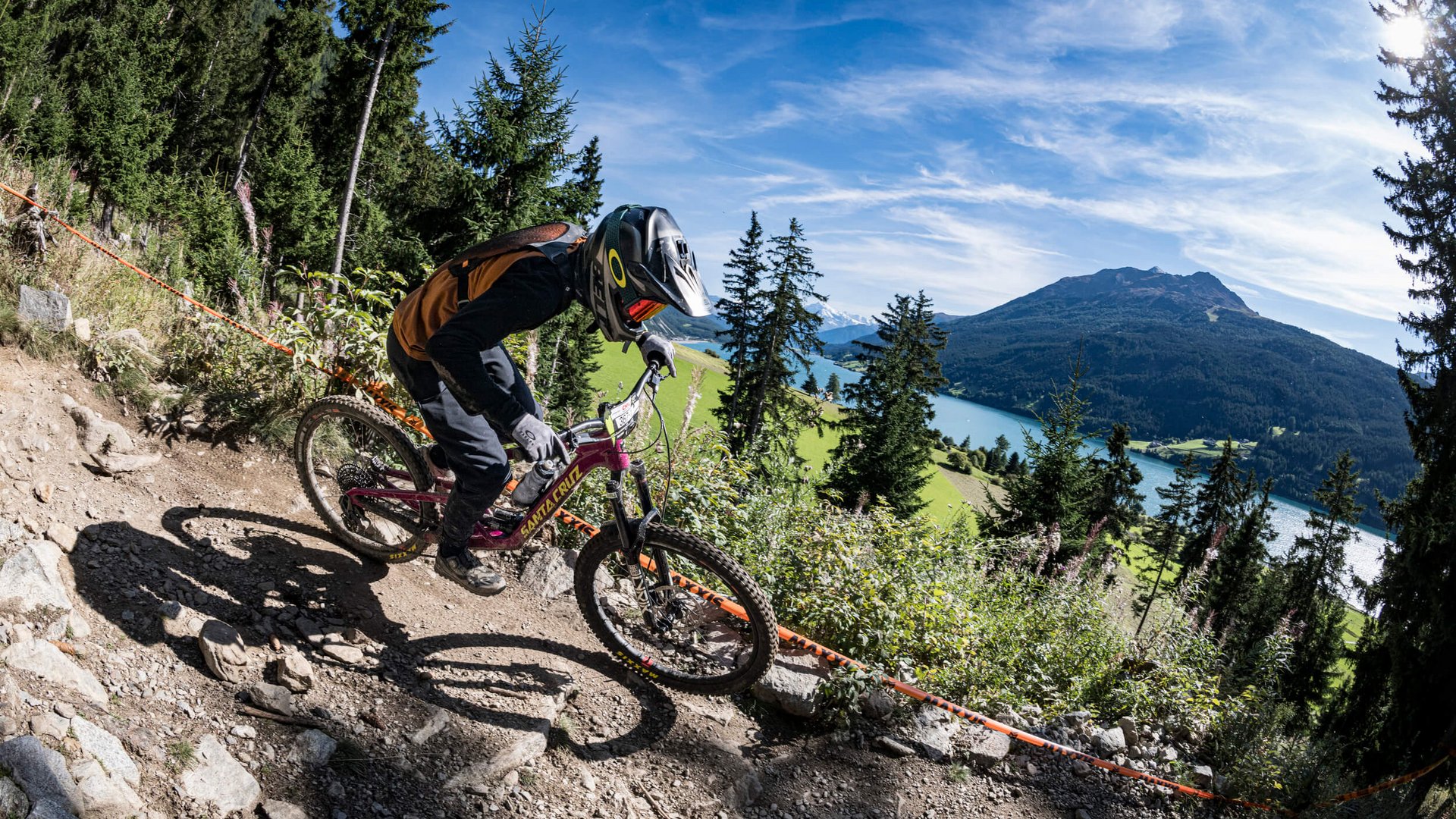 Green Days in Nauders-Reschensee © Manfred Stromberg Mountainbiker fährt auf felsigem Waldweg mit Berg und See im Hintergrund