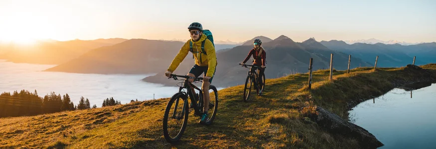 Zwei Mountainbiker fahren bei Sonnenaufgang auf einem Hügel mit Bergsicht
