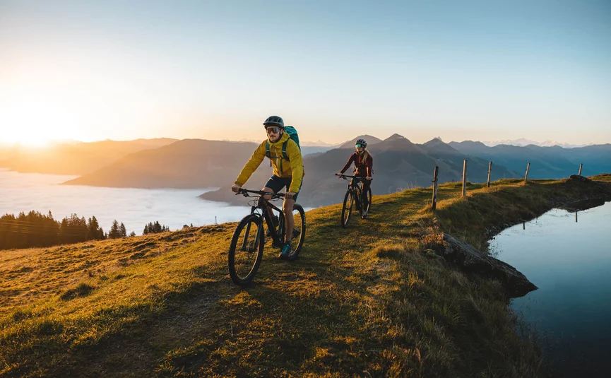 Zwei Mountainbiker fahren bei Sonnenaufgang auf einem Hügel mit Bergsicht