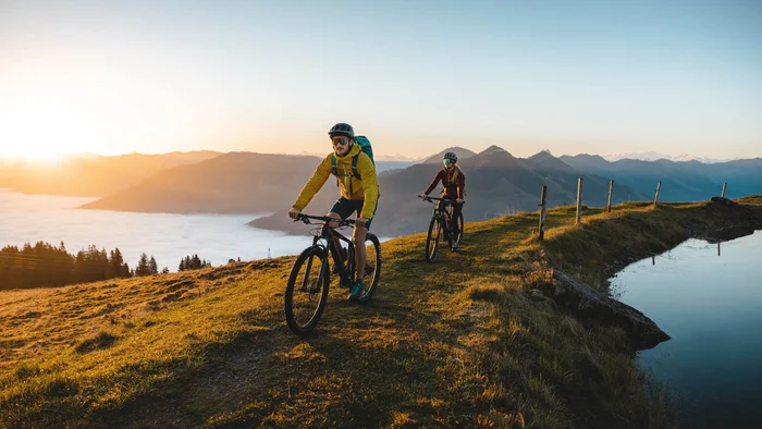 Twee mountainbikers fietsen bij zonsopgang op een heuvel met bergzicht