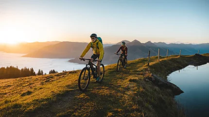 Zwei Mountainbiker fahren bei Sonnenaufgang auf einem Hügel mit Bergsicht