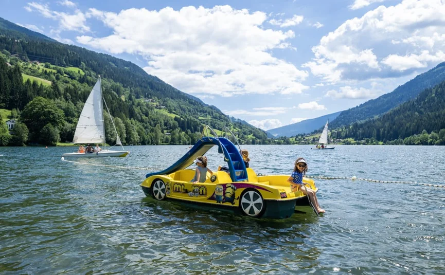 Happy Family week Kids on yellow pedal boat with slide on lake with sailboats and mountains