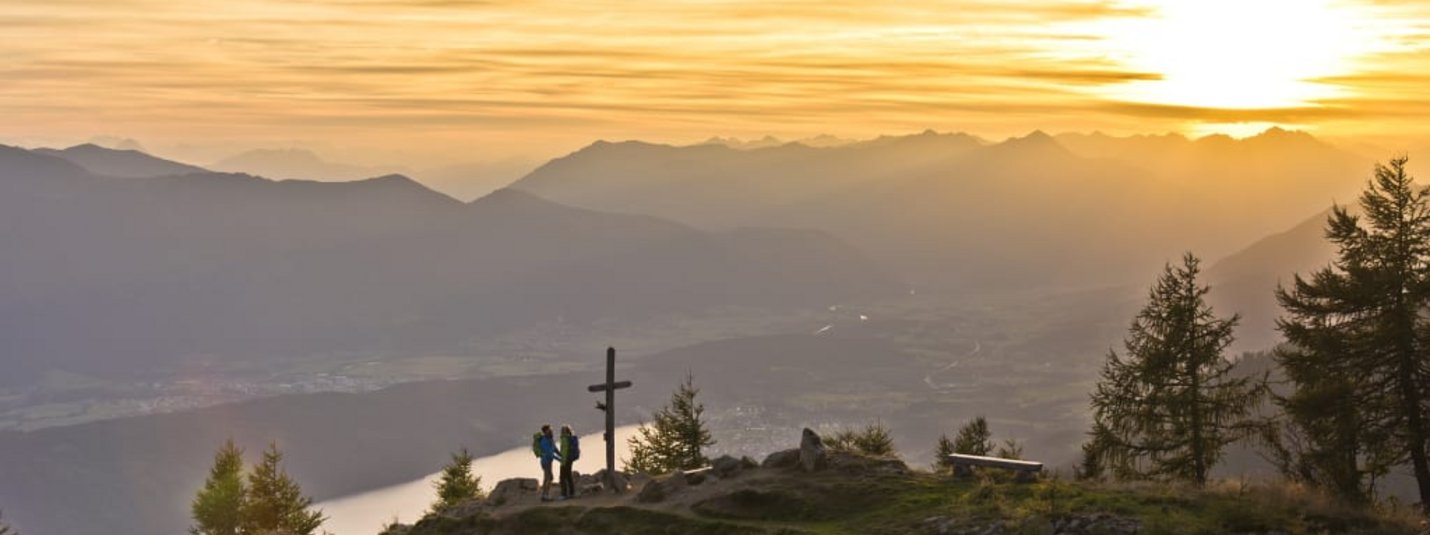 Kurztrip- Wanderlust in den Nockbergen Twee wandelaars bij topkruis bij zonsondergang in de bergen