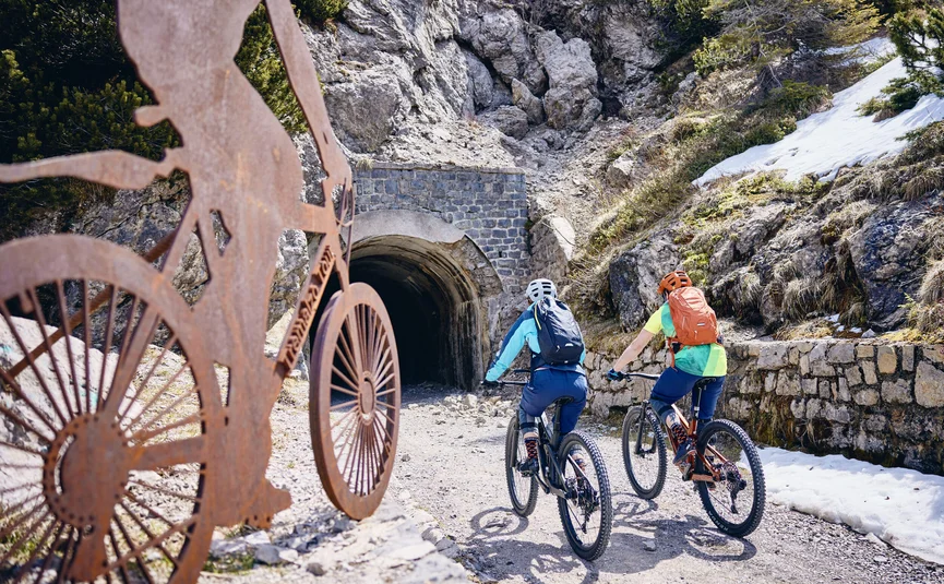 Zwei Radfahrer fahren auf Trail auf Tunnel in bergiger Landschaft zu