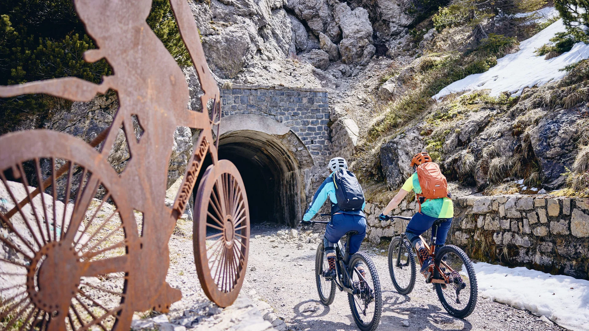 Zwei Radfahrer fahren auf Trail auf Tunnel in bergiger Landschaft zu