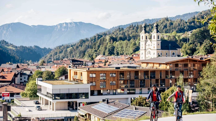 Zwei Menschen fahren Mountainbike vor Alpenstadt mit Kirche und Bergen