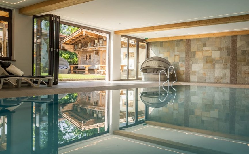 Indoor swimming pool with glass walls overlooking rustic garden house